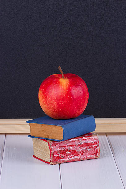 istock Red apple on old mini book against blackboard 607961654