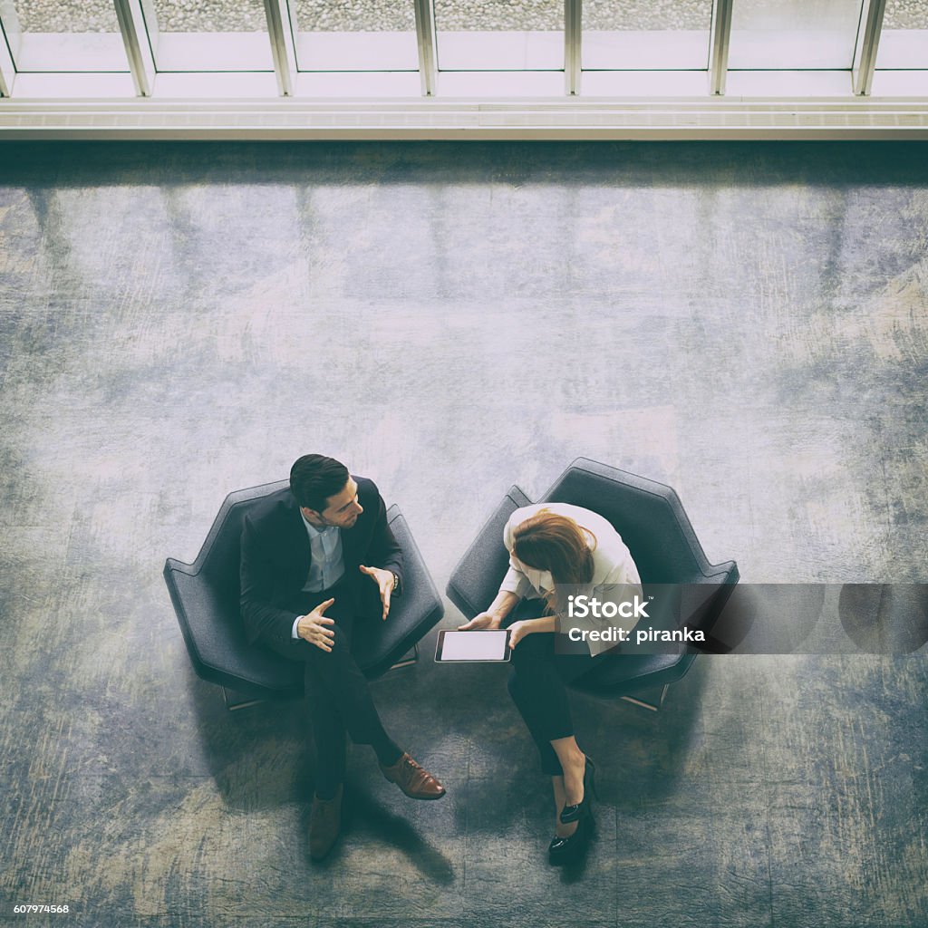 Overhead view of two business persons in the lobby A high-angle view of a businessman and a businesswoman sitting in the office building lobby and using a digital tablet Business Stock Photo