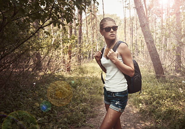 Young active female with backpack walking through summer forest. Concept of vacation and adventure.