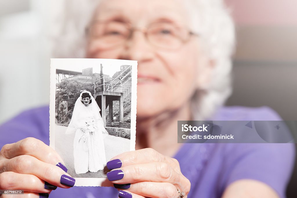 Senior Woman Holding Her Wedding Photo An 89 year old woman holding a photo of herself as a young bride. Senior Adult Stock Photo