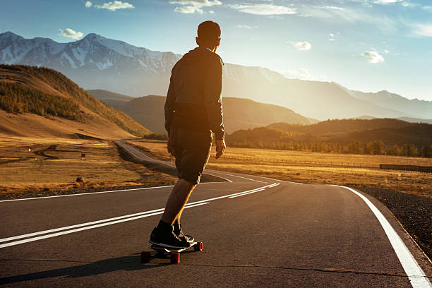 Man rides on longboard at sunset Man rides at straight road on longboard at sunset time longboarding stock pictures, royalty-free photos & images
