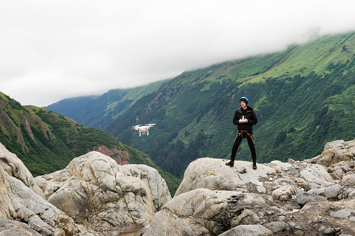 Young adult male in 20s flies a drone over the rocky moraine landscape at the terminus of a glacier while on a trekking adventure on Lemon Glacier, Juneau Icefield, Juneau, Alaska, USA