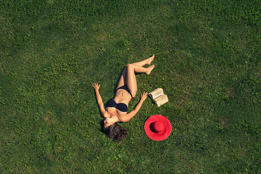 Woman lying on the grass near sunbed with book