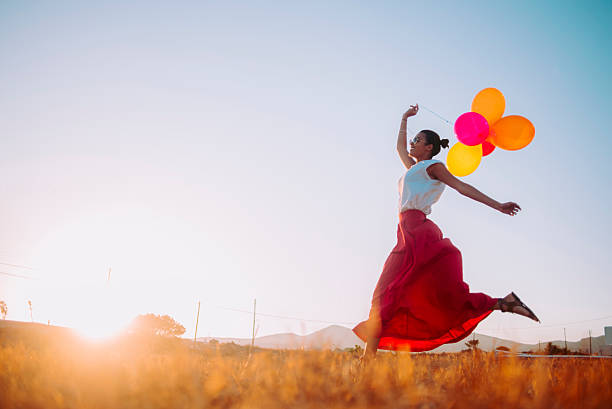 young woman running threw the fields holding balloons stock photo