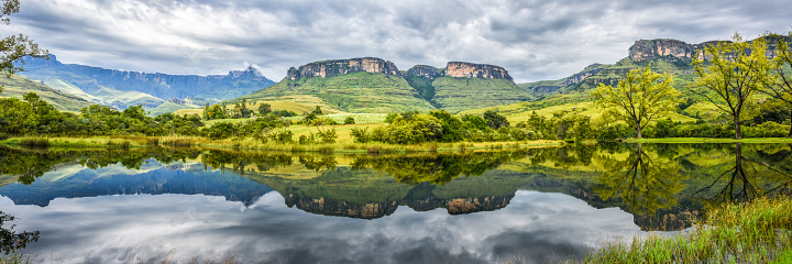flat top mountains and green lush hills reflected in water on cloudy day, panorama.