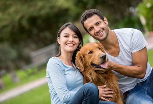 Portrait of a happy couple with their dog at the park and looking at the camera smiling