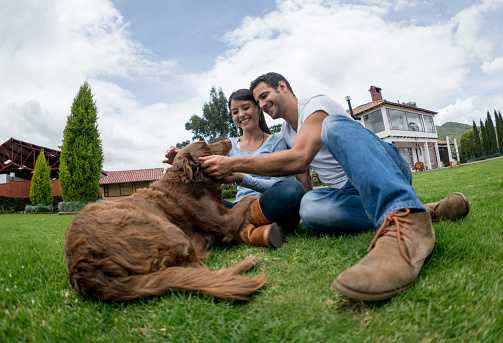 Happy couple pampering their dog and relaxing outdoors in the backyard of their house - lifestyle