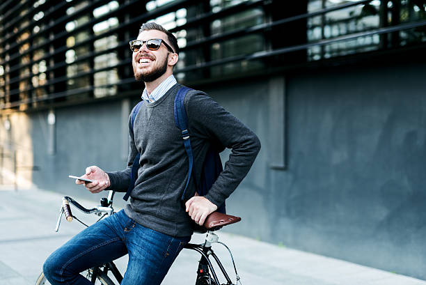 Taking a quick break Shot of a businessman using his cellphone while going to work with his bicycle. hipster bike stock pictures, royalty-free photos & images