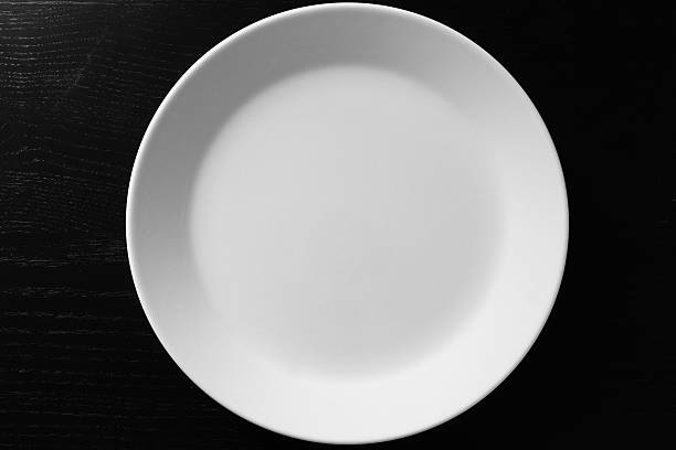 Empty white plate on black wooden table Empty white plate on black wooden table. Kitchen tools close up spinning top stock pictures, royalty-free photos & images