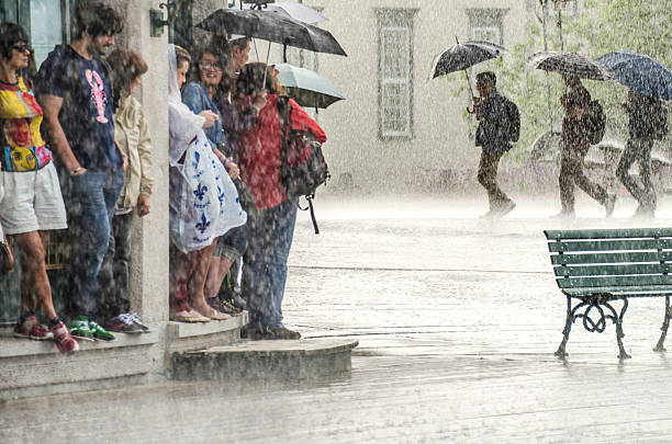 um grupo de pessoas se esconde da chuva forte debaixo de um prédio. - chuva torrencial - fotografias e filmes do acervo