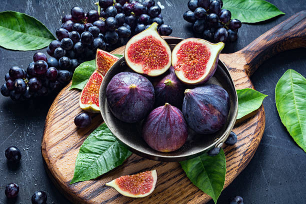 Fresh ripe figs and black grapes on wooden chopping board. Concept of freshness, healthy food, fresh fruits, summer market harvest and colors.