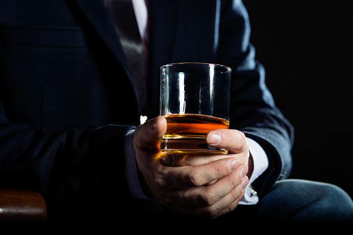 Closeup of serious businessman holding glass of whisky illustrate executive privilege concept.