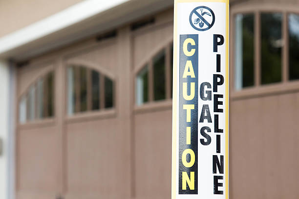 Caution gas pipeline sign near a home garage A post with a sign on it cautions that there is a gas pipeline. The gas pipeline is in front of the brown garage door on a house in this Colorado residential neighborhood. gas pipeline marker stock pictures, royalty-free photos & images