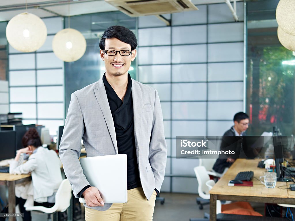 portrait of young asian entrepreneur young asian entrepreneur standing in office with laptop computer under arm. Japanese Ethnicity Stock Photo