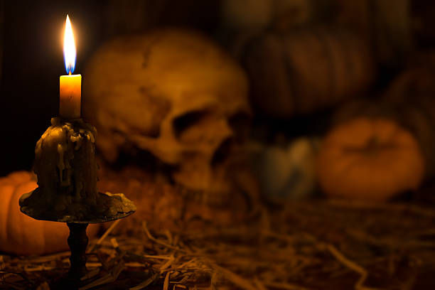 Still life art of wizard wooden desk with skull of lighting candle and books with glasses on with a pencil in in dark blue tone background, concept of wisdom in the dark