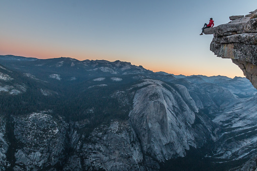 Adventurer sitting at the summit of the top Half Dome in California. At his feet the precipice and the wonderful views accompany him.