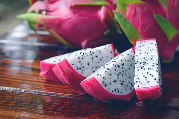 Pink skin dragon fruit with white meat and black seed sliced on wooden background.
