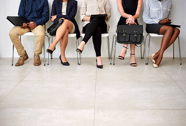 Getting an interview is a foot in the door Shot of a group of businesspeople seated in line while waiting to be interviewed cross legged stock pictures, royalty-free photos & images