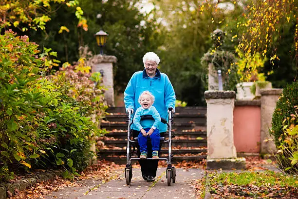 Happy senior lady with a walker or wheel chair and children. Grandmother and kids enjoying a walk in the park. Child supporting disabled grandparent. Family visit. Generations love and relationship.
