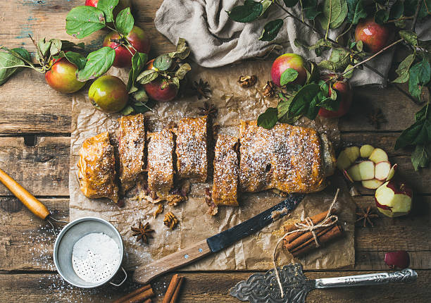 Apple strudel cake with cinnamon, nuts and sugar powder Apple strudel cake with cinnamon and sugar powder cut in slices served with star anise, nuts and fresh apples on rustic wooden background, top view, horizontal composition strudel stock pictures, royalty-free photos & images