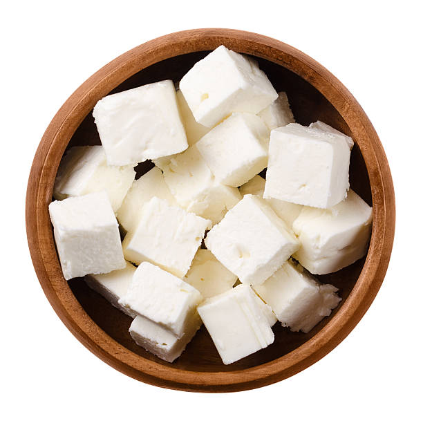 Greek Feta cheese cubes in wooden bowl over white Greek Feta cheese cubes in a wooden bowl on white background. Cubes of a brined curd white cheese made in Greece from milk of sheeps and goats. Crumbly aged cheese with slightly grainy texture. curd cheese photos stock pictures, royalty-free photos & images