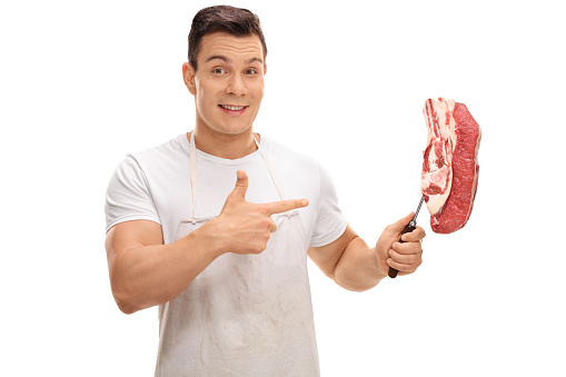 Smiling butcher holding a fork with a steak and pointing isolated on white background