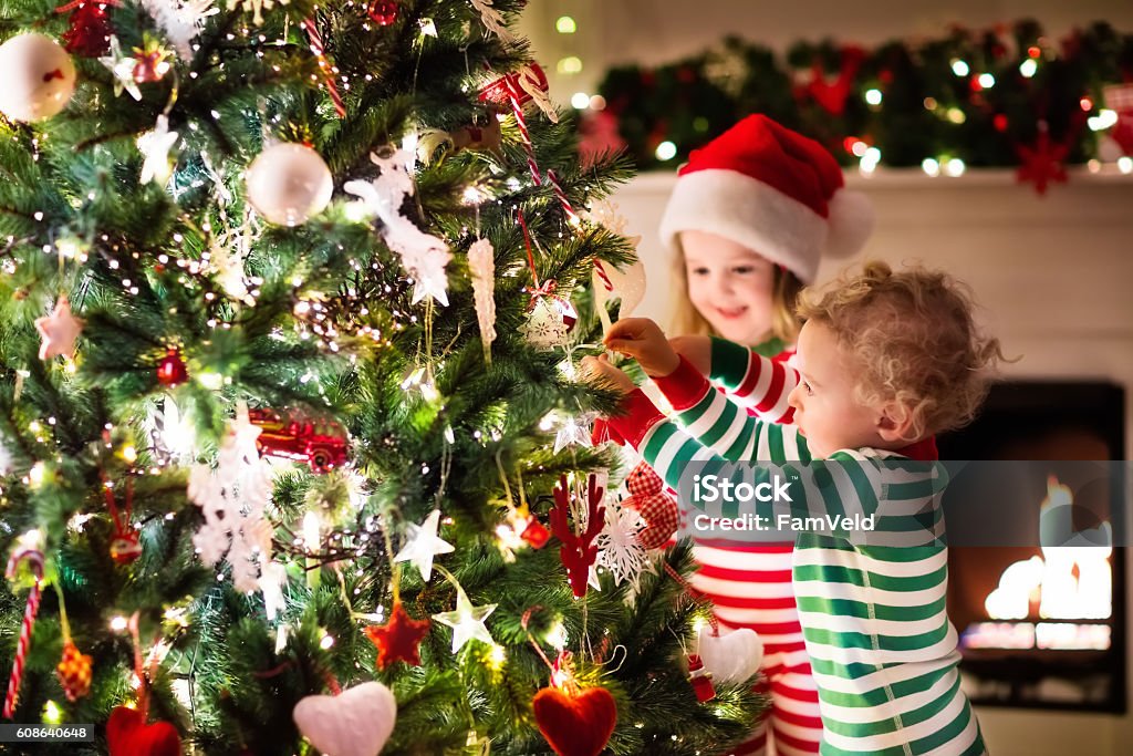 Kids decorating Christmas tree in beautiful living room Happy little kids in matching red and green striped pajamas decorate Christmas tree in beautiful living room with traditional fire place. Children opening presents on Xmas eve. Christmas Stock Photo