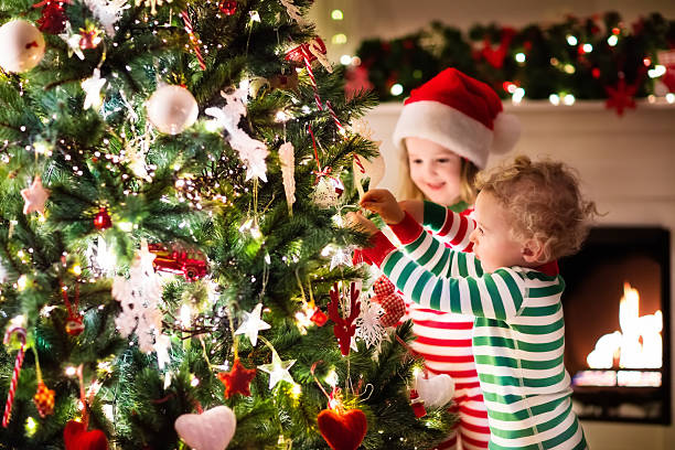 Kids decorating Christmas tree in beautiful living room Happy little kids in matching red and green striped pajamas decorate Christmas tree in beautiful living room with traditional fire place. Children opening presents on Xmas eve. decorating stock pictures, royalty-free photos & images