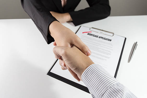 Businessman and businesswoman handshake over the approved mortgage application stock photo