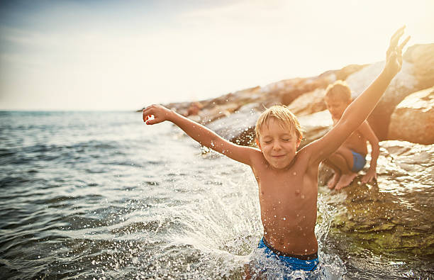 Kids jumping into the sea from big stones Two little brothers aged 7 are having fun in sea.  Kids are jumping into the sea from big stones. Sunny summer day in Tuscany, Italy. wave jumping stock pictures, royalty-free photos & images