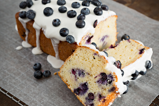 A high angle extreme close up of a partially sliced, freshly baked and frosted blueberry loaf