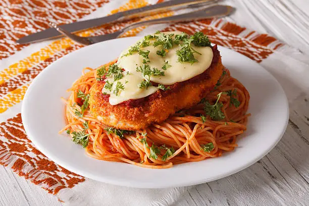 Chicken Parmigiana and pasta with tomatoes close-up on a plate on the table. horizontal
