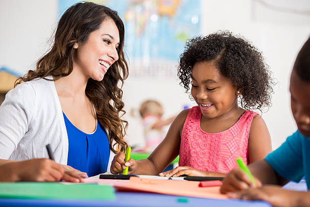 istock Cheerful teacher helping preschool student with art project 609049614