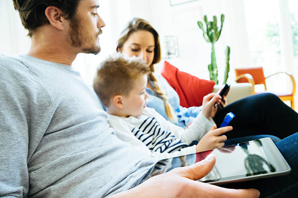 リビングルームで一緒に技術を使用して陽気な若い家族 - gamer watching tv adult couple ストックフォトと画像