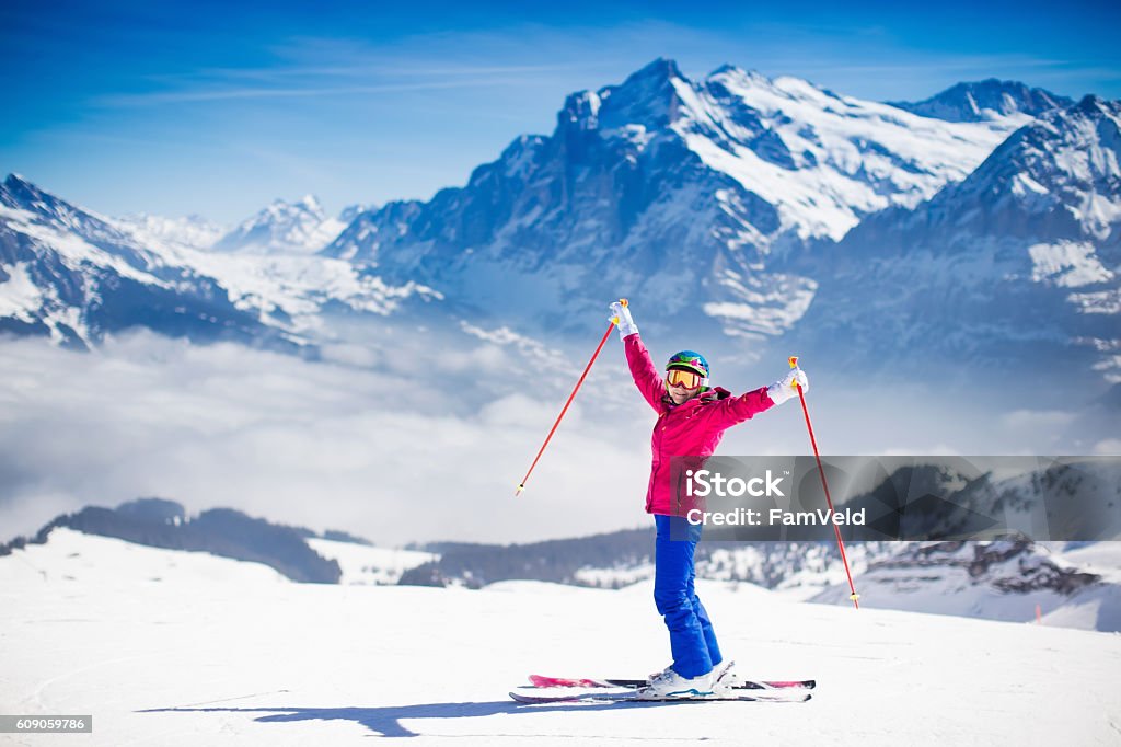 Young active woman skiing in the mountains. Young active woman skiing in mountains. Female skier kid with safety helmet, goggles and poles enjoying sunny winter day in Swiss Alps. Ski race for adults. Winter and snow sport in alpine resort. Skiing Stock Photo