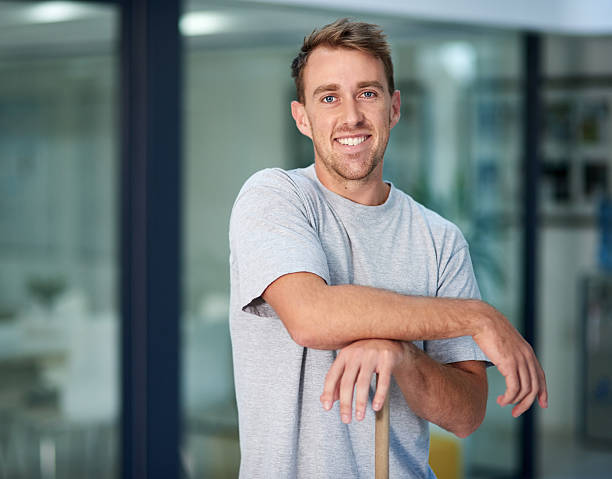 Portrait of a young man leaning on a mop while cleaning the office floor