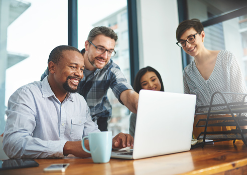 Cropped shot of a group of colleagues working together on a laptop in a modern office