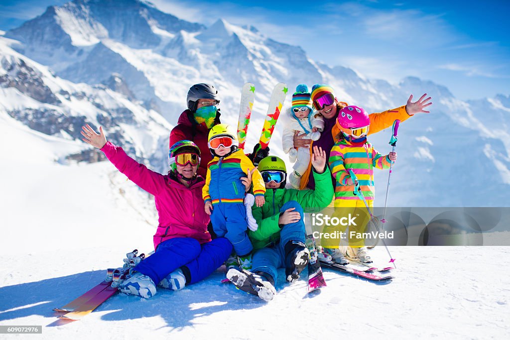 Family with kids in the mountains Family ski vacation. Group of skiers in Swiss Alps mountains. Adults and young children, teenager and baby skiing in winter. Parents teach kids alpine downhill skiing. Ski gear and wear, safe helmets. Skiing Stock Photo
