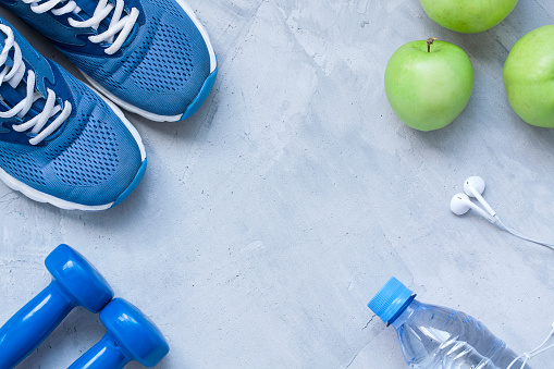 Flat lay sport shoes, dumbbells, earphones, apples, bottle of water on gray concrete background. Concept healthy lifestyle, sport and diet. Selective focus. Flat lay shot of Sport equipment.