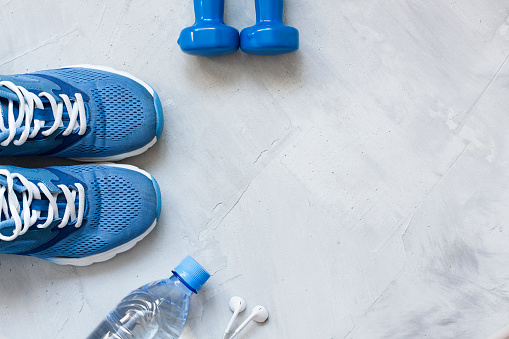 Flat lay sport shoes, bottle of water, dumbbells and earphones on gray concrete background. Concept healthy lifestyle, sport and diet. Focus is only on the sneakers. Sport equipment.