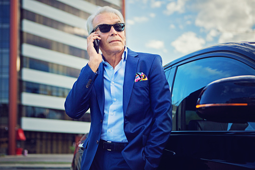 Businessman is talking using his mobile phone standing next to his car