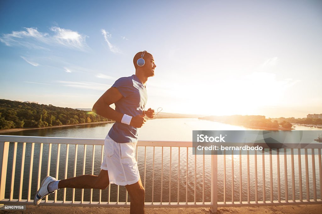 Beautiful sunset run A young man running on the bridge along a river. Lens flare, warm tones. Running Stock Photo