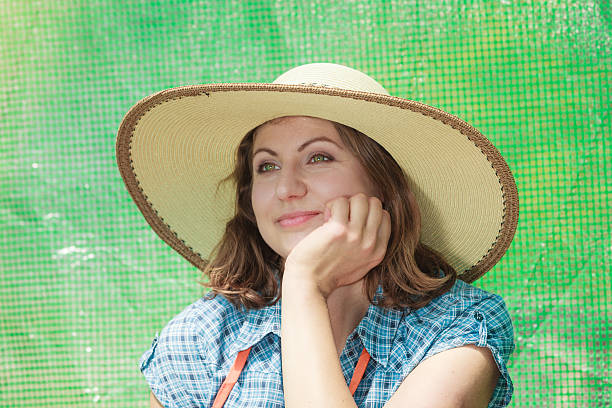Portrait of mature thoughtful woman wearing big straw hat in garden greenhouse