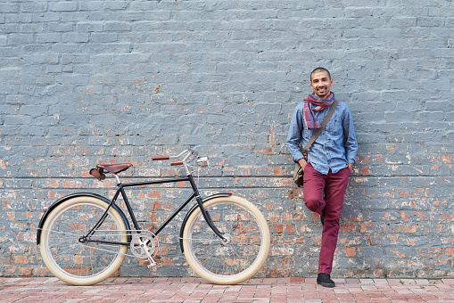 Portrait of a young man posing with his bicycle against a grey wall in the city