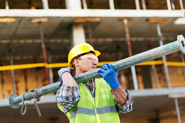 travailleur transportant des barres de support en acier sur le chantier de construction - heavy work photos et images de collection