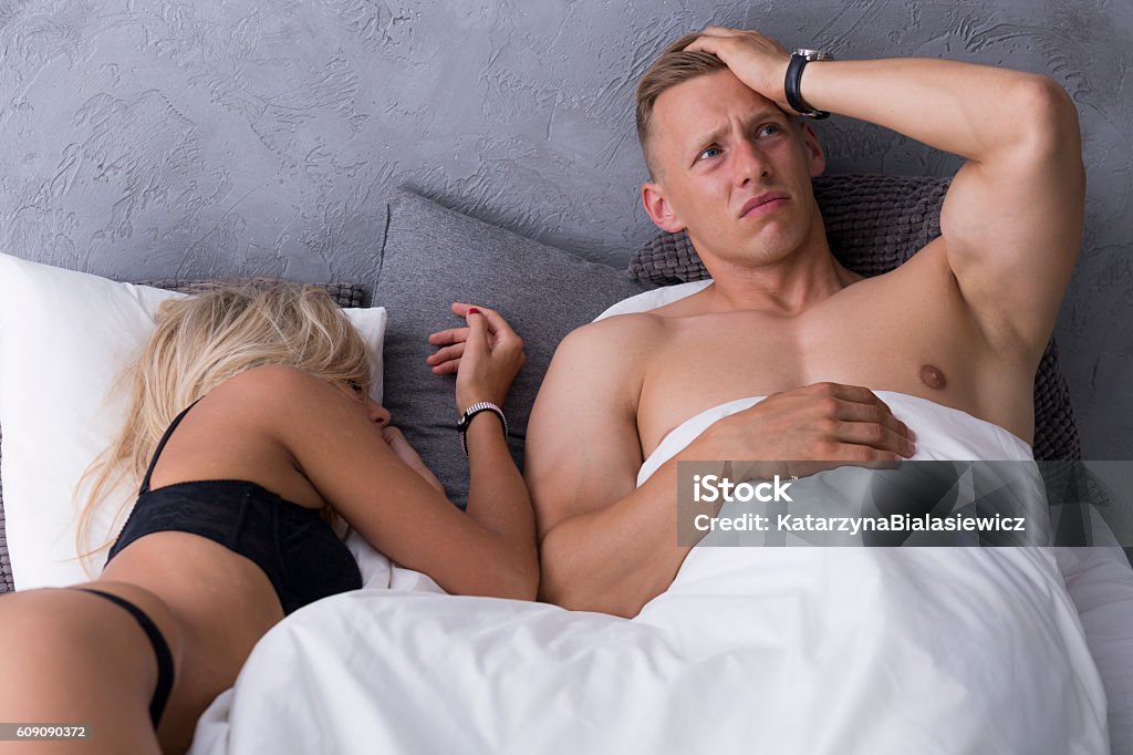 What happened last night...? Man with a hangover lying in a hotel bed with sexy woman in a black underwear Evil Stock Photo