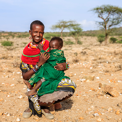 Young African mother from Samburu tribe carrying her baby , Kenya, Africa. Samburu tribe is one of the biggest tribes of north-central Kenya, and they are related to the Maasai.