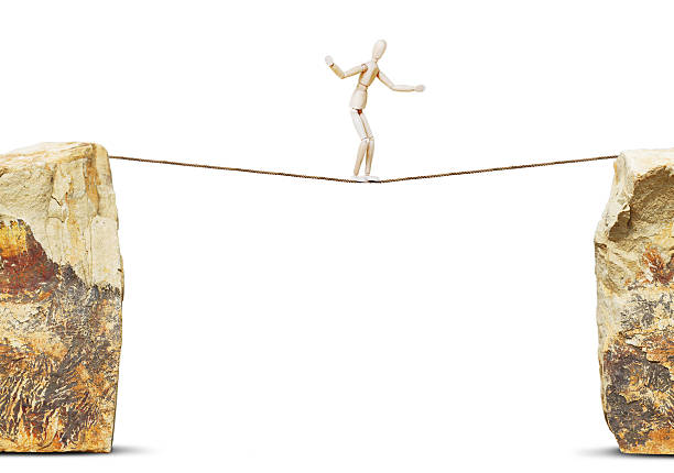 Man goes along a rope between high rocks. Concept of danger with a wooden puppet