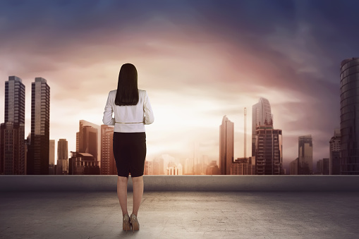 Asian business woman on the roof and looking at the city with skyscrapers enjoy sunset