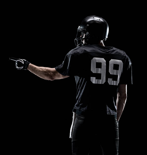 Rear view of American football player pointing Rear view of American football player pointing american football player studio stock pictures, royalty-free photos & images